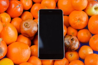Cep telefonunda en iyi görünümü kadar taze mandalina portakal doğal fruites arka plan üzerinde sahte. Modern dijital aygıt düz yatıyordu tasarım