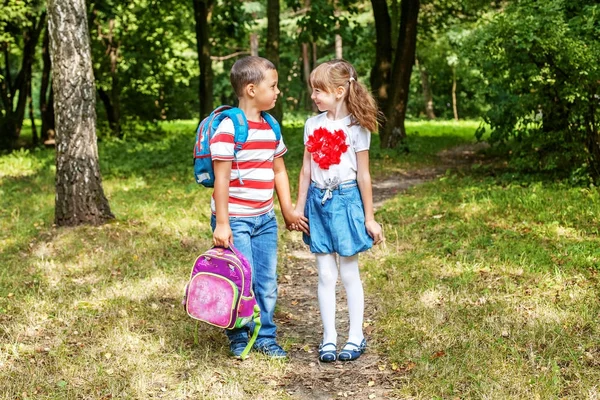 As crianças dão as mãos. O menino está carregando uma mochila para uma menina . — Fotografia de Stock