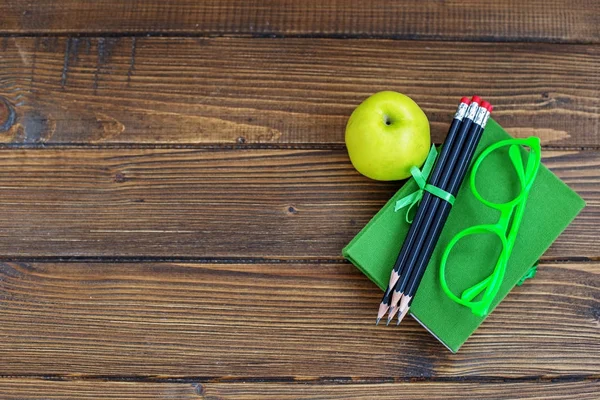 Pencils and glasses, a book and a delicious apple on a wooden ba