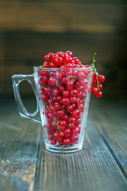 Kırmızı kuş üzümü ile cam fincan. Ahşap arka plan.