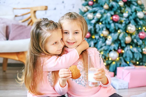 Children drink milk and eat oatmeal cookies. Girls hugging.