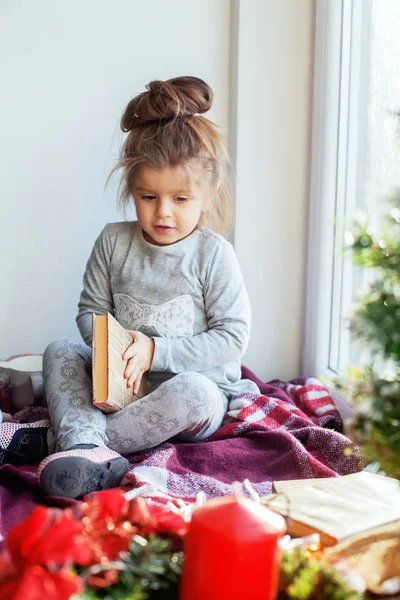 Dziecko czyta książkę na parapecie. Pojęcie Boże Narodzenie — Zdjęcie stockowe