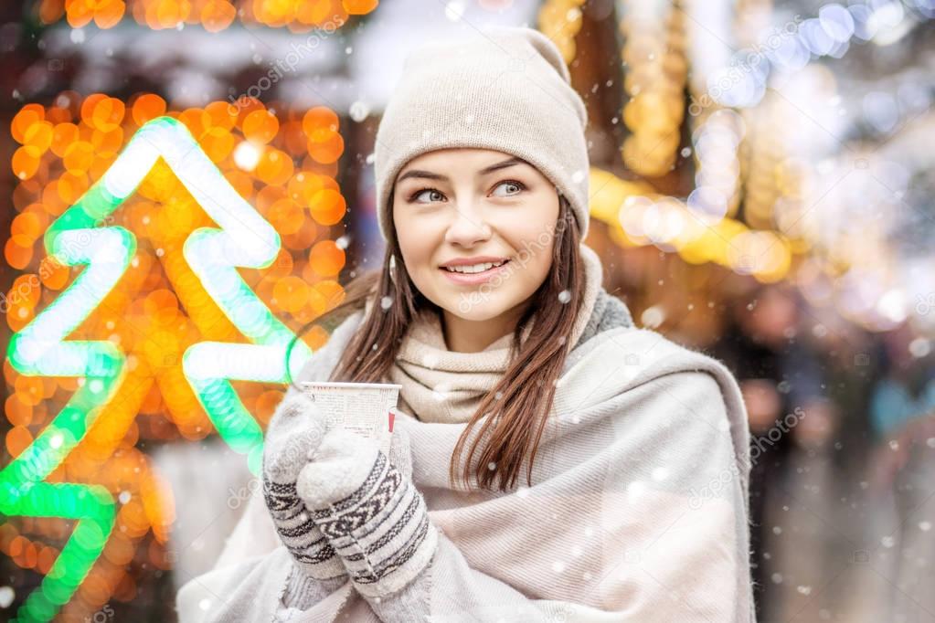 A cheerful woman drinks coffee on the street. Snow. Copy Space. 