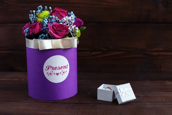 Красиві квіти в фіолетовій коробці з кільцями на дерев'яному фоні . — стокове фото