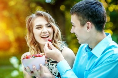 Genç aşıklar birkaç kiraz yiyor. Parkta gülüyor. 