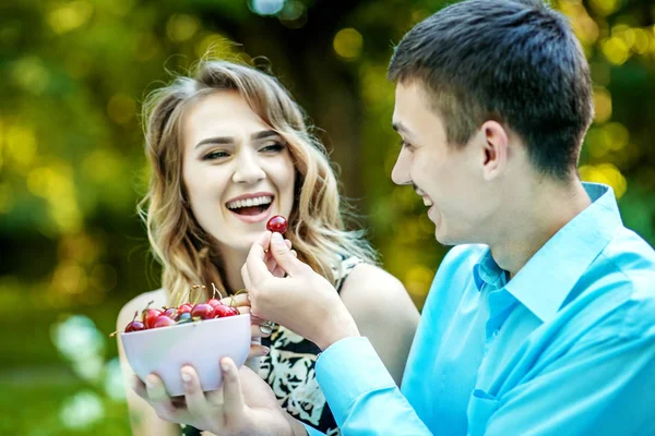 Унг мальчик и девочка едят вишни. Смех в парке . — стоковое фото