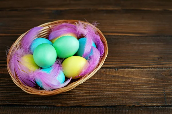 Färgade ägg med fjädrar i en korg på en trä bakgrund. C — Stockfoto