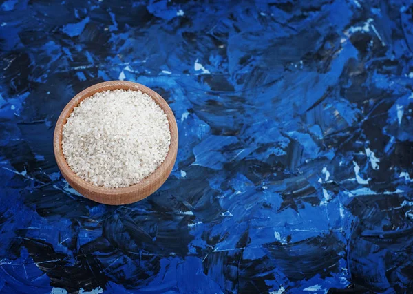 Arroz crudo en un tazón sobre un fondo azul. Ingrediente. Vista superior. T — Foto de Stock