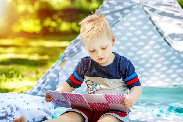 En liten unge läser en bok i parken. Pojke förskola. — Stockfoto