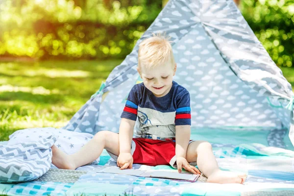 Egy kis gyerek nevet, és elolvassa a könyvet, a parkban. — Stock Fotó