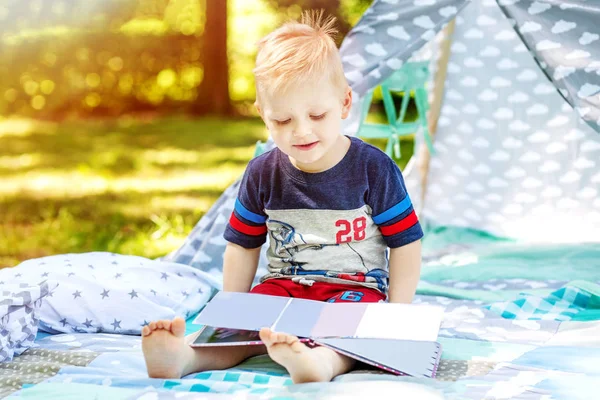 Ett lyckligt barn läser en bok i parken. Pojke förskola. Sommar. — Stockfoto