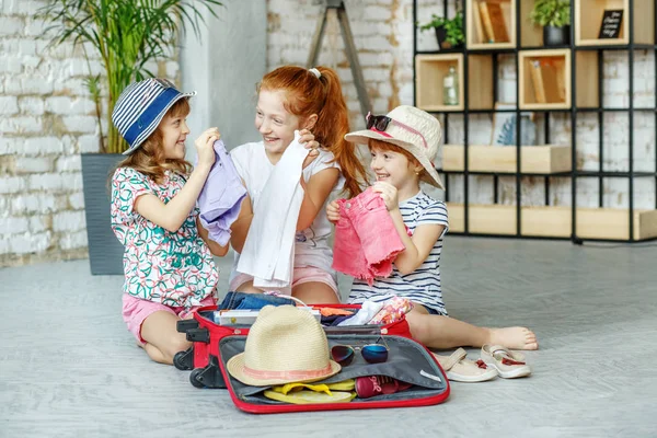 Drie kleine meisjes verpakt hun kleren in een koffer. Concept, — Stockfoto