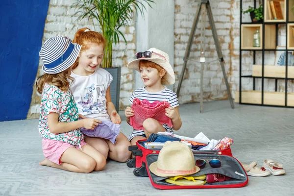 Трое счастливых детей упаковывают свою одежду в чемодан. Концепция , — стоковое фото