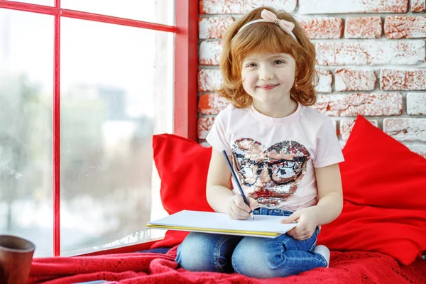 A cheerful child writes and sits on a window sill. The concept i — Stock Photo, Image