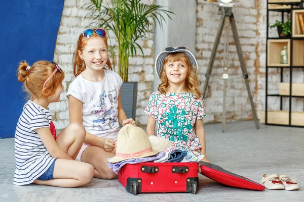 Трое счастливых детей девочек собирают чемодан в поездку. Концепция — стоковое фото