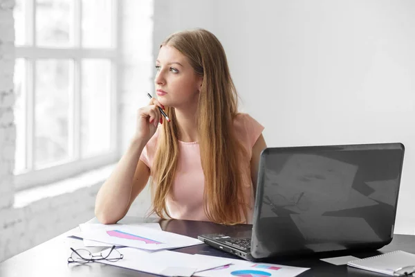 Una giovane donna adulta si siede e pensa ad una scrivania. Il concetto di business, lavoro e fare soldi . — Foto Stock