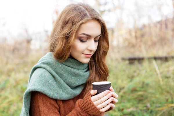 Young adult woman in a brown knitted sweater. Coffee in a plastic glass. The concept of a lifestyle, autumn, art, cosmetics and care. Nature. The concept of a lifestyle, autumn, cosmetics and care. — Stock Photo, Image