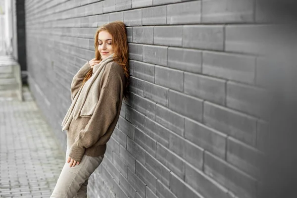 Mulher adulta bonita fica perto de uma parede preta. Camisola de malha marrom. Conceito de moda, estilo de vida, urbano e outono . — Fotografia de Stock