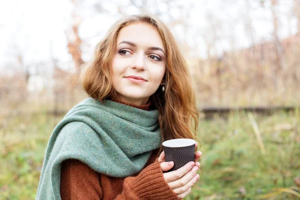 Jeune femme adulte en pull marron tricoté. Café dans un verre en plastique. Le concept d'un style de vie, automne, art, cosmétiques et soins. La nature. Le concept d'un style de vie, automne, cosmétiques et soins . — Photo