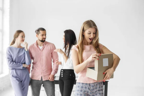 Una mujer abre una caja de regalo y admira. Un grupo de empleados. El concepto de saludos y regalos para la Navidad . —  Fotos de Stock