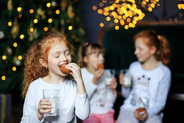 Дети пьют молоко и едят печенье в канун Рождества. Сестры в пижаме. Концепция счастливого Рождества, праздников, семьи и подарков . — стоковое фото