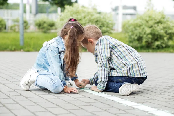 Little friends draw with chalk on the pavement. The concept of childhood, back to school, friendship.