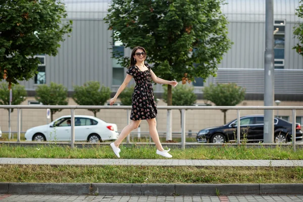 Взрослая улыбающаяся женщина скачет по улице в стильном платье. Концепция образа жизни, городской и активной жизни . — стоковое фото