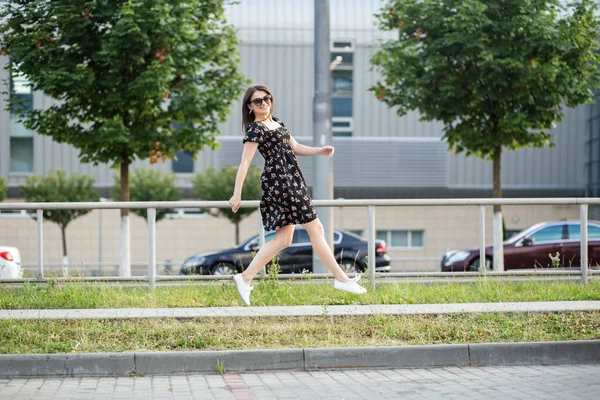 大人のブルネットの女性がスタイリッシュなドレスで通りを走っています。生活様式、都市生活様式、活動的生活様式の概念. — ストック写真