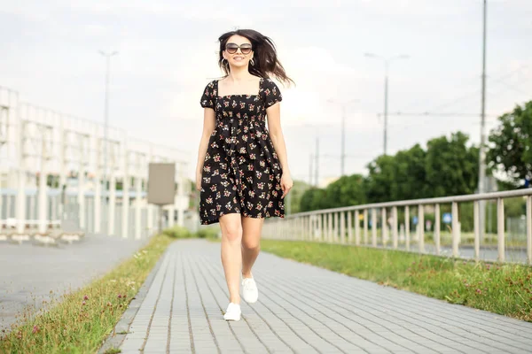 Chica sonriente adulta está caminando por la calle en un vestido de verano. El concepto del estilo de vida, la vida urbana y activa . — Foto de Stock