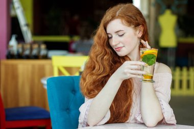 Mutlu kızıl saçlı kız kafede lezzetli meyve çayı içiyor. Yaşam tarzı, içki ve sağlıklı yemek kavramı..