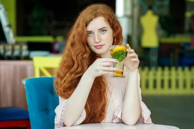 Kızıl saçlı mutlu kız kafede lezzetli kokteyller içer. Yaşam tarzı, içki ve sağlıklı yemek kavramı..