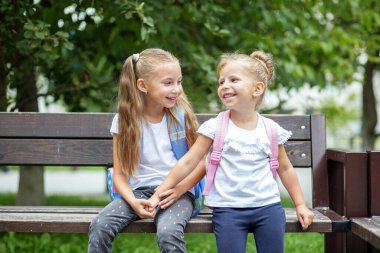 İki küçük çocuk bankta gülüp sohbet ediyor. Sırt çantalı kızlar. Konsept okula, aileye, arkadaşlığa ve çocukluğa geri döndü..