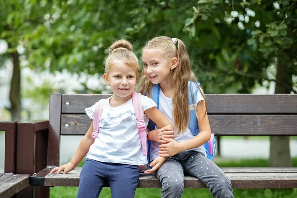 Två Små Barn Skvallrar Bänk Tjejer Med Ryggsäckar Konceptet Tillbaka — Stockfoto