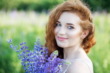 Kızıl saçlı kıvırcık kadın gülümsüyor ve elinde lupin çiçekleri tutuyor. Güzel makyaj malzemesi. Yavaş yaşam, organik kozmetik ve dijital detoks kavramları.