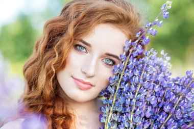 Kızıl saçlı kıvırcık kadın elinde lupin çiçeği tutuyor. Yakın plan. Yavaş yaşam, organik kozmetik ve dijital detoks kavramları.