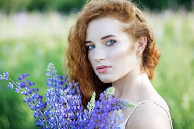 Kızıl saçlı kıvırcık kadın elinde lupin çiçeği tutuyor. Güzel makyaj malzemesi. Yavaş yaşam, organik kozmetik ve dijital detoks kavramları.