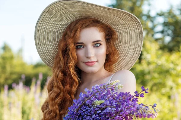 Kızıl saçlı kıvırcık kadın elinde lupin çiçeği tutuyor. Hasır şapka. Yavaş yaşam, organik kozmetik ve dijital detoks kavramları.