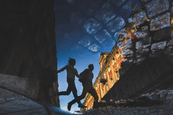Running guy and girl in reflection in puddle — Stock Photo, Image