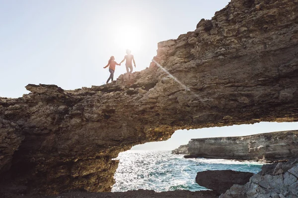 Silhouette couple running by rocky coast — Stock Photo, Image