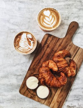 İki taze gevrek tereyağı kruvasan ahşap plaka ve iki sıcak cappuccino