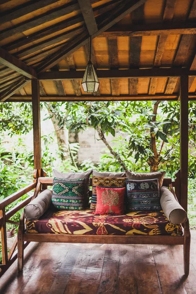 Wooden sofa with pillows on terrace under roof in ethnic style with colorful traditional ornaments — Stock Image Wooden Sofa Pillows Terrace Roof Ethnic Style Colorful Traditional Ornaments Stock Photo