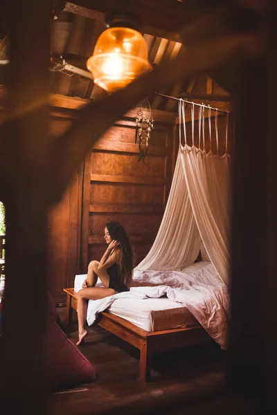 妇女穿着黑色内衣坐在床上的民族木制房子上午 — 图库照片