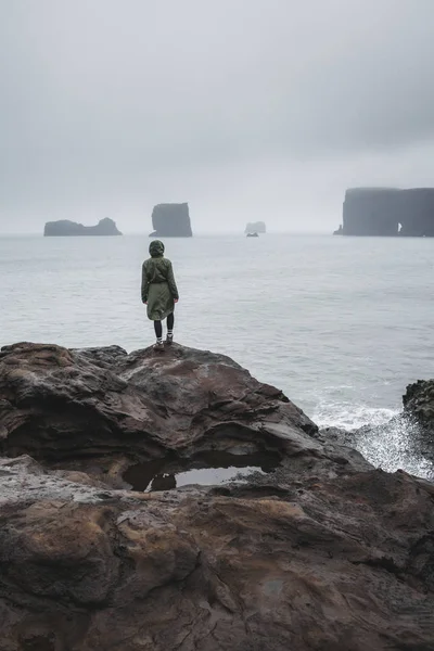 穿着卡其布夹克站在黑色火山岩海滩上的人 — 图库照片