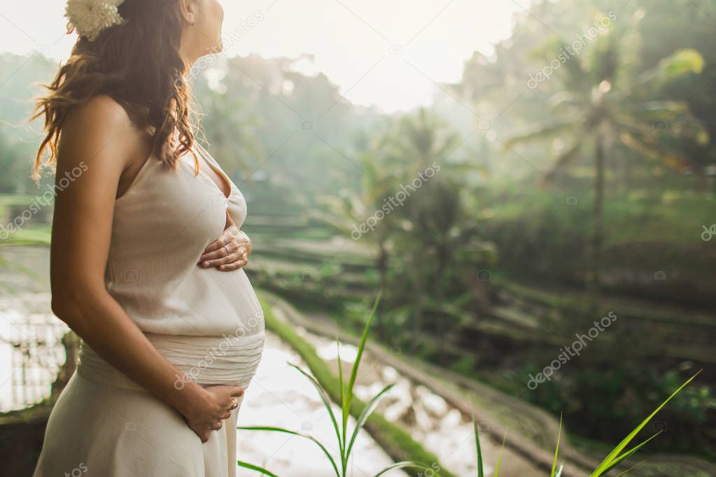 Young pregnant woman in white dress with view of Bali rice terra