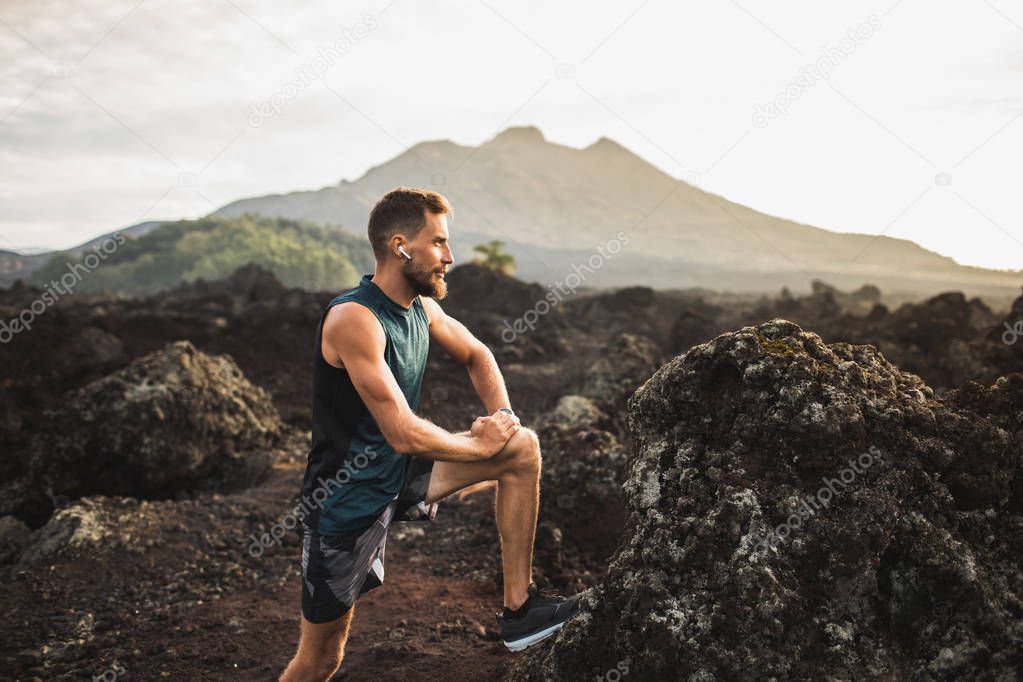 Young hipster runner with beard stretching and warming-up for tr