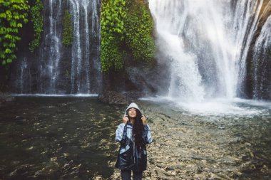 Bali 'de şelalenin keyfini çıkaran genç ve mutlu bir kadın. Gri yağmurlu
