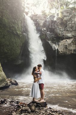 Genç çift öpüşürken harika bir Tegenungan manzarası var.