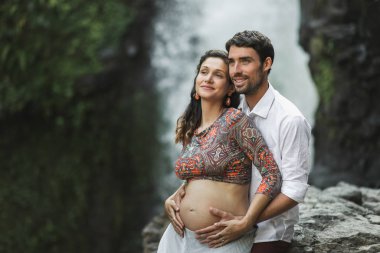 Young pregnant couple in love with amazing view of  Tegenungan c clipart