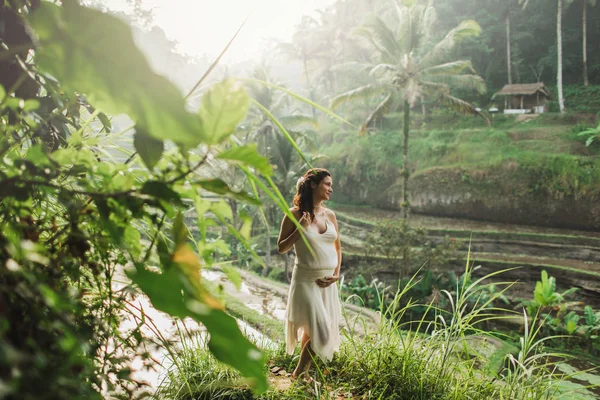 身穿白衣、望着巴厘岛稻田的年轻孕妇 — 图库照片