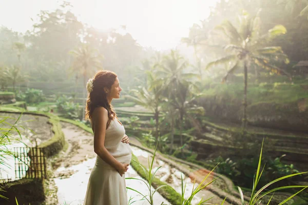 身穿白衣、望着巴厘岛稻田的年轻孕妇 — 图库照片